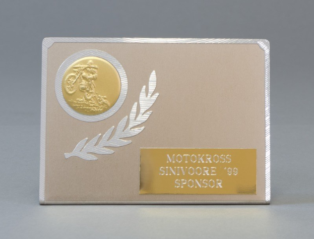 Goldene und silberne Visitenkarte mit Lorbeerkranz-Design, mittig im Bild mit Text, der wahrscheinlich den Namen des Sponsors angibt.