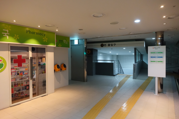 Der Eingang zu einer Apotheke mit einem Schild, auf dem "Apotheke" steht, auf der linken Seite, einer Tafel mit Text auf der rechten Seite und beleuchteten Lampen auf dem Dach.