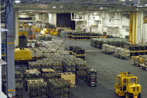 Ein großes Lagerhaus voller Numerous Trucks, Container, Menschen, Lichter, Stangen und andere Gegenstände mit einem sichtbaren Rad.