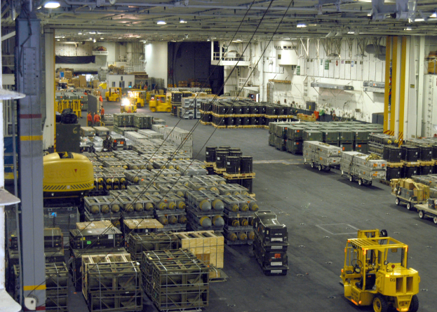 Ein großes Lagerhaus voller Numerous Trucks, Container, Menschen, Lichter, Stangen und andere Gegenstände mit einem sichtbaren Rad.