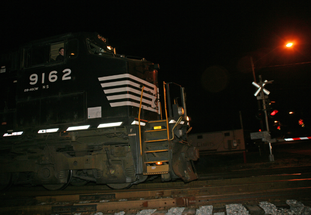 Ein Zug auf Schienen mit einer roten Lampe an einem Pfahl auf der rechten Seite, vor einem dunklen Hintergrund.