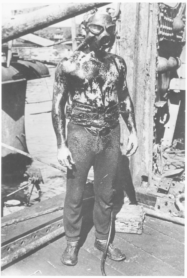 Ein altes Schwarz-Weiß-Foto eines Mannes in einer Gasmaske und Schuhen auf dem Deck eines Schiffs, bereit zur Erkundung des Ozeans.