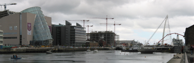 Ein Fluss mit Schiffen, eine Brücke, Geböude, Baukröne und der Himmel im Hintergrund.