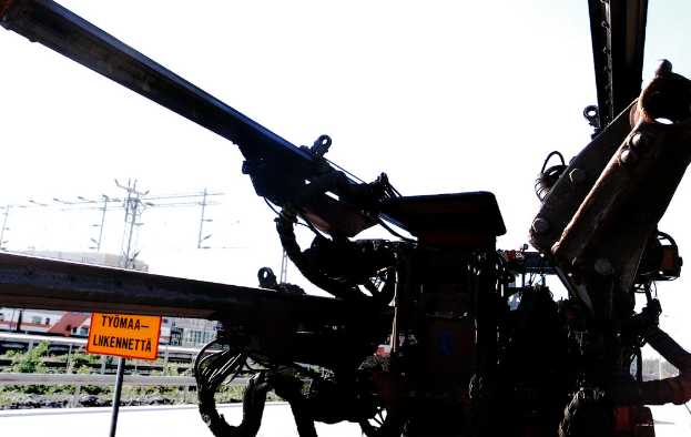 Eine Maschine ist im Vordergrund mit Strommasten, Kabeln, Absperrungen, Pflanzen und Himmel im Hintergrund positioniert.