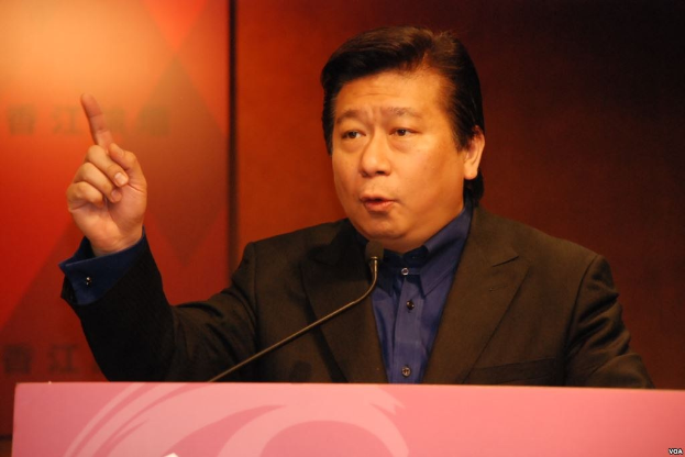 Ein Mann in Anzug und Krawatte, der eine Rede an einem Rednerpult mit einem Mikrofon hält und wie ein Politologe mit ernster Miene wirkt.