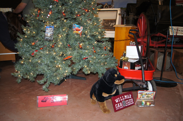 Eine Szene mit einem Hundespielzeug, Namensschildern, einem Einkaufswagen mit Gegenständen, einem Weihnachtsbaum, einem Rad, einem Pfahl, einer Kette, einer Holzplatte, einer Person, die steht, und verschiedenen anderen Gegenständen im Hintergrund.