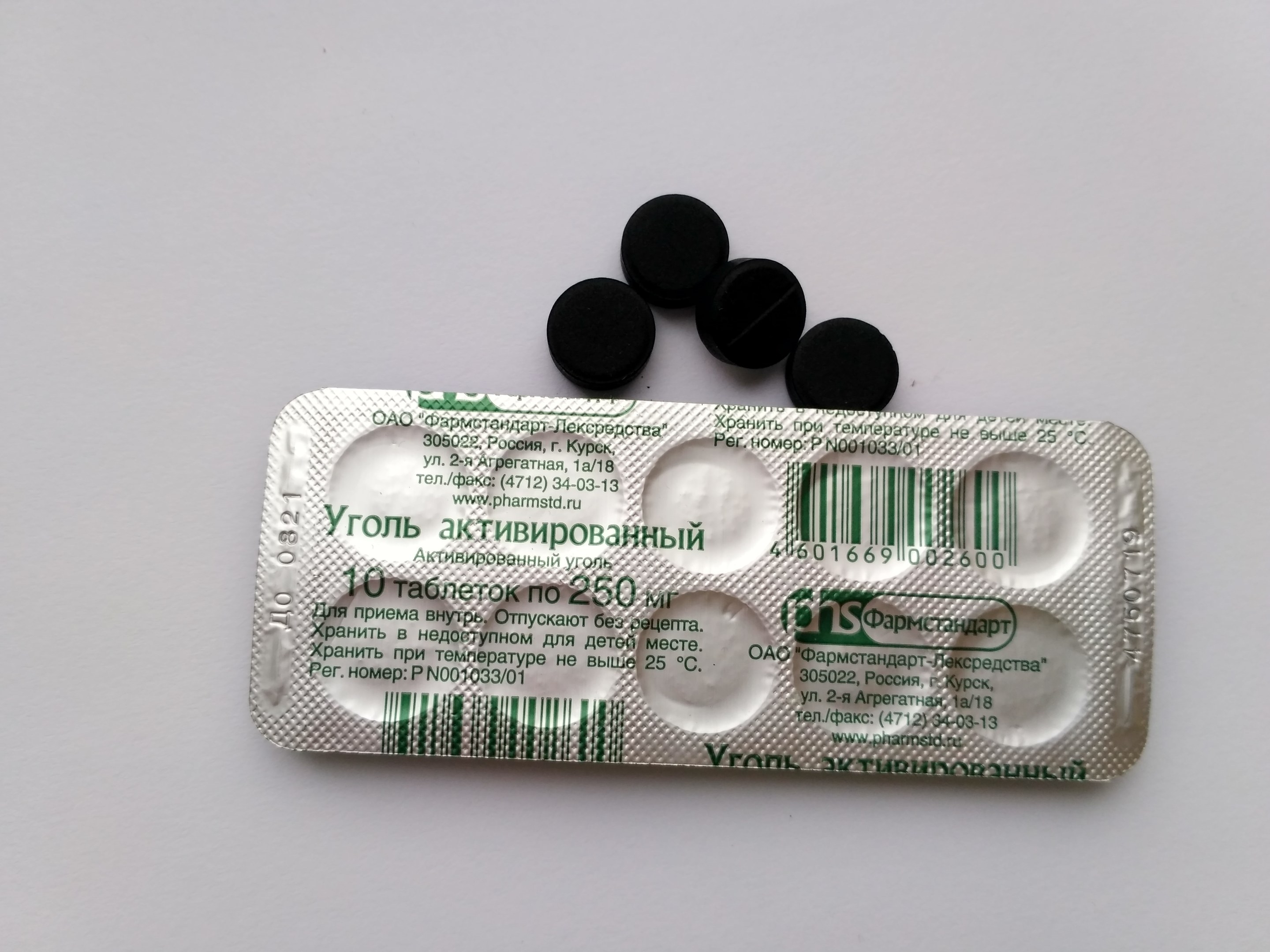 Weißer Tisch mit einer Blisterpackung schwarzer Pillen, mit Text und einem Barcode, daraufgestellt.