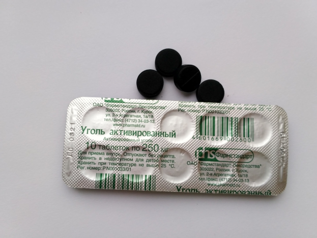 Weißer Tisch mit einer Blisterpackung schwarzer Pillen, mit Text und einem Barcode, daraufgestellt.