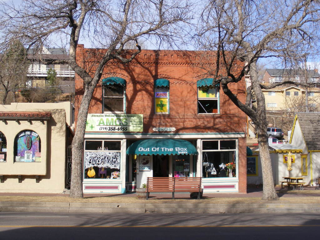 Eine Straße mit Gebäuden, Bänken, Bäumen, einem Fahrzeug und dem Himmel im Hintergrund.