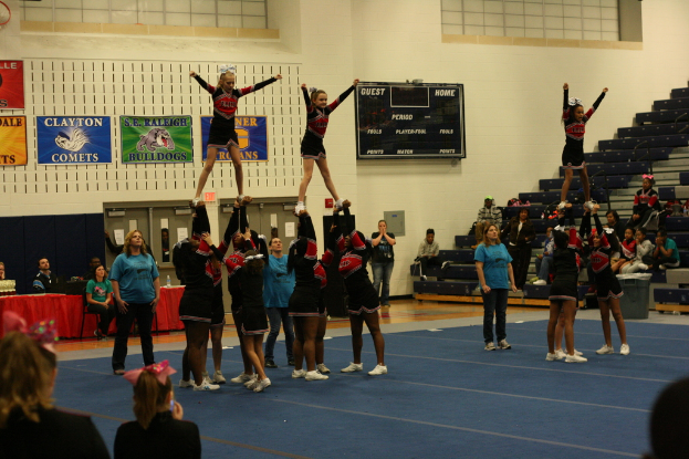 Menschen in verschiedenen Uniformen befinden sich auf einem Boden mit einer schwarzen Scorecard, Treppe und einem Tisch mit roter Decke.