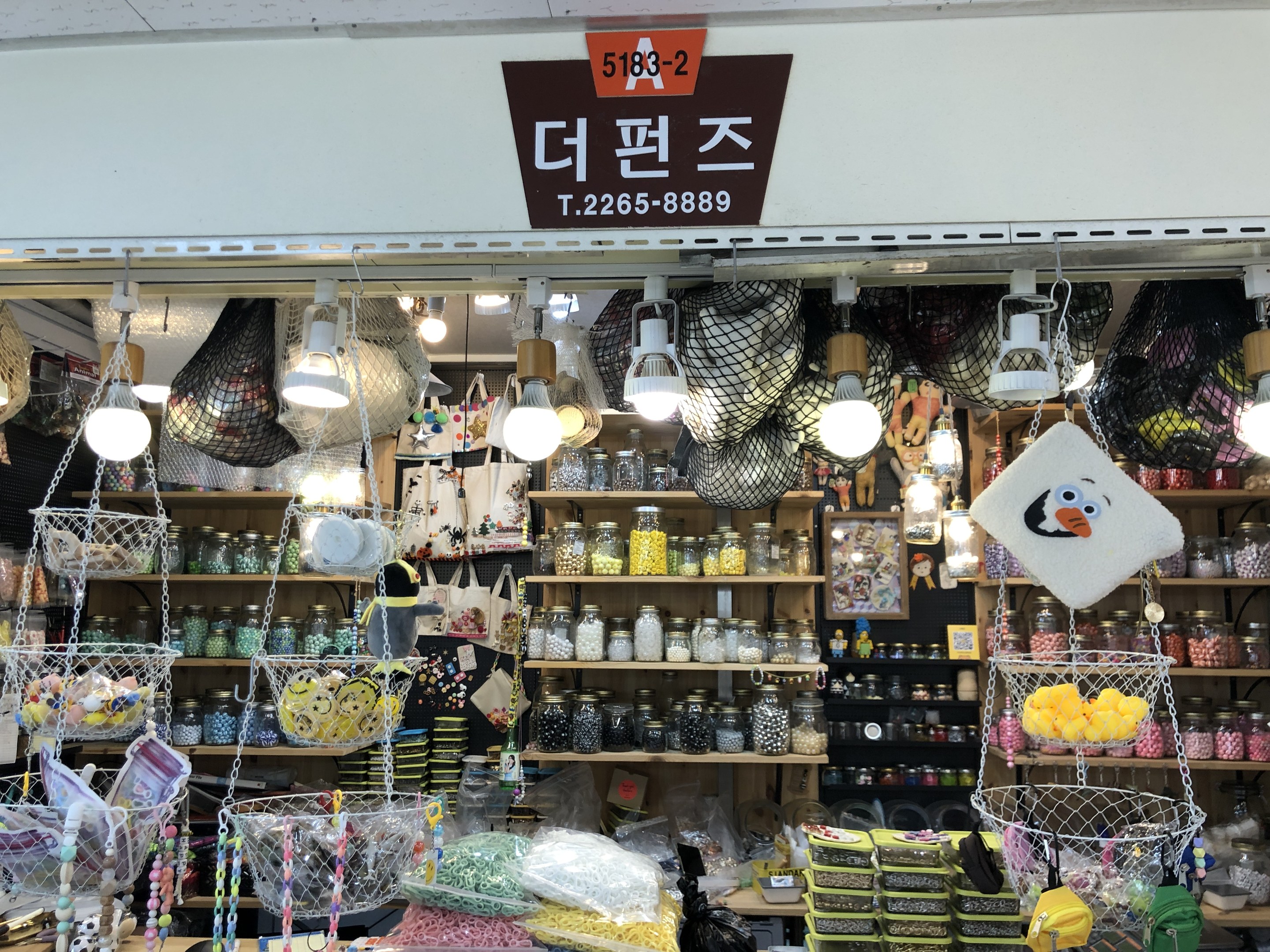 Ein unordentlicher Ladeneinrichtungsdisplay mit verschiedenen Gegenständen wie Körpfen, Lichtern, Flaschen und Spielzeugen auf Gestellen, mit einer Tafel öber dem Display, die es als eines der besten koreanischen Geschäfte in Seoul angibt.