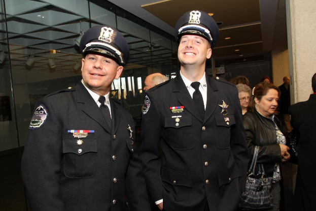 Zwei strahlende Beamte im Vordergrund, mit Menschen in der Mitte, Glasfenster links, Lampen und Decke oben und Säulen und Menschen rechts.