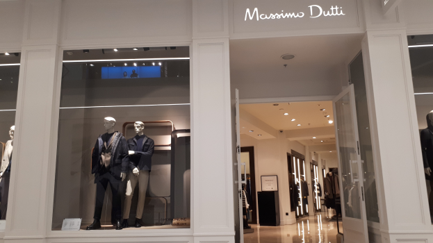 Vitrine des Massimo Dutti in Mailand, Italien mit Schaufensterpuppen in moderner Kleidung, Innenbeleuchtung und Texttafeln.