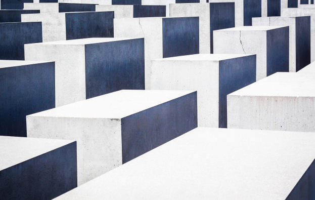 Luftaufnahme des Holocaust-Mahnmals für die ermordeten Juden Europas in Berlin, mit zahlreichen weißen und blauen Betonsteinen in einem Gittermuster angeordnet.