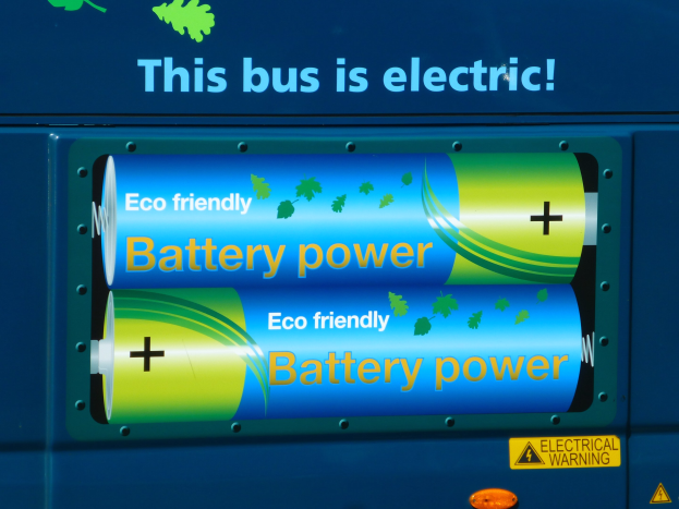 Ein blauer Elektrobus mit einer Tafel, auf der "Dieser Bus ist elektrisch" steht, und zwei Batterien an der Seite.