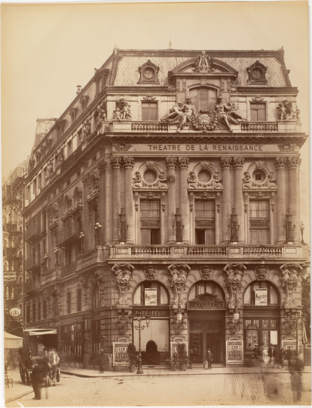 Ein altes Foto des Théâtre de la Renaissance in Paris, Frankreich, das ein Gebäude mit Fenstern, Säulen, Bögen und Skulpturen an der Fassade zeigt, mit ein paar Menschen und Fahrzeugen auf der Straße davor und dem Himmel im Hintergrund.