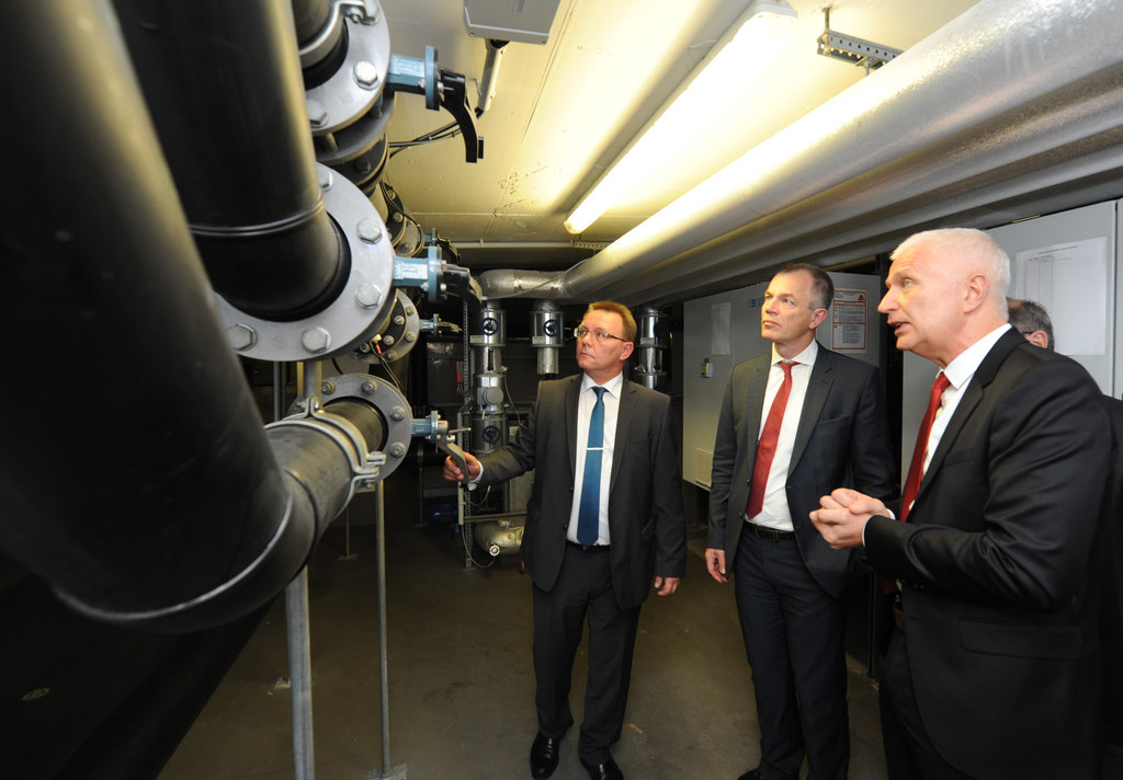 Vier Personen auf der rechten Seite, drei mit Mänteln, mit großen Rohrleitungen auf der linken Seite.