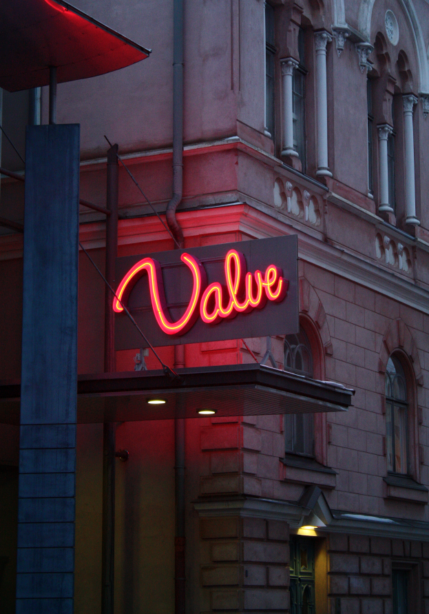 Ein Gebäude mit Fenstern, einer Tür, einem Pfahl und einer neonfarbenen "Valve"-Leuchtschrift.