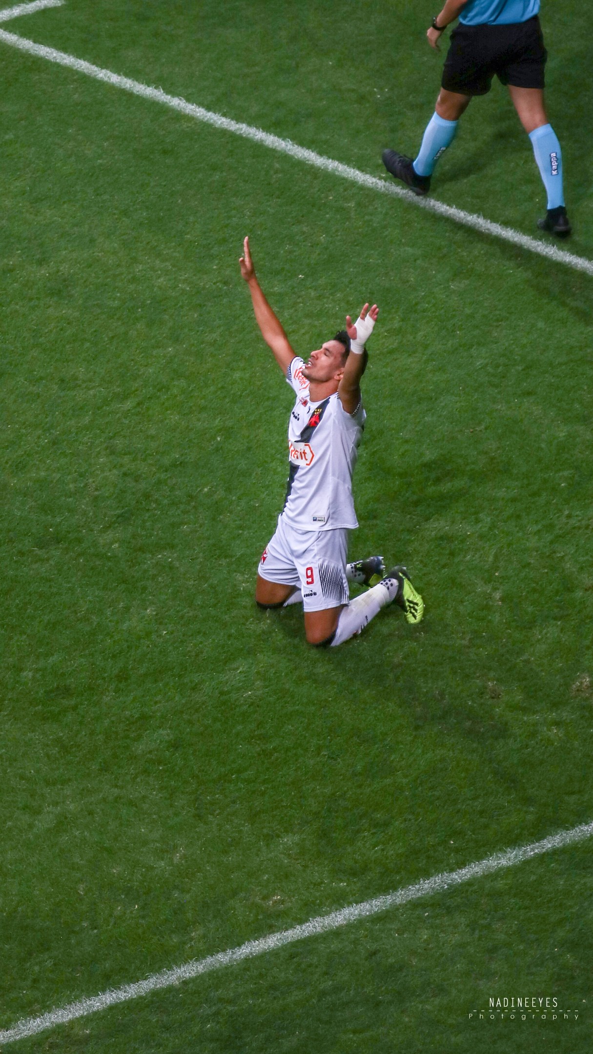 Ein Fußballspieler kniet auf dem Boden mit ausgestreckten Armen in Feierlaune, trägt einen Sportanzug und Fußballschuhe.