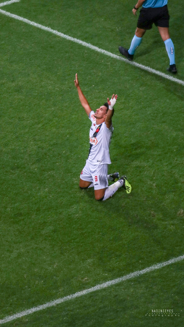 Ein Fußballspieler kniet auf dem Boden mit ausgestreckten Armen in Feierlaune, trägt einen Sportanzug und Fußballschuhe.