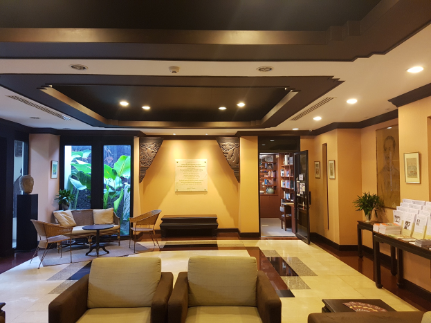 Ein gut beleuchteter Hotelfoyer mit Sitzbereichen mit Sofas und Stühlen, Tischen, Zimmerpflanzen, Bücherregalen, Deckenleuchten, Wanddekorationen und Beistelltisch-Dekoration, entworfen zum Entspannen mit ausreichend natürlichem Licht.