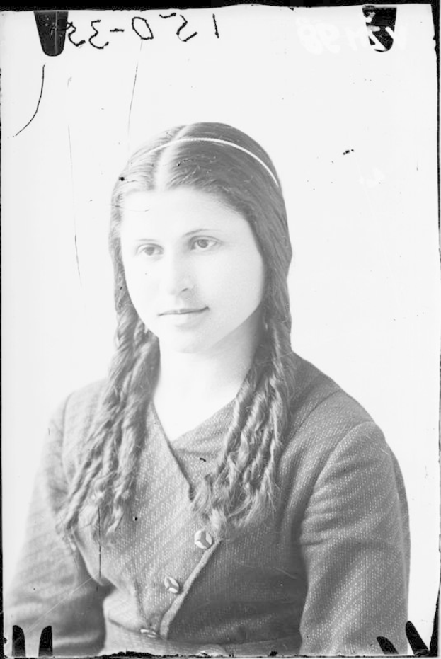 Ein Schwarz-Weiß-Porträt von Julia Margaret Cameron, einer Frau mit langen Zöpfen, die ein weißes Kleid und einen gemusterten Schal trägt und einen sanften Ausdruck hat und ihre Hände vor der Brust verschränkt.