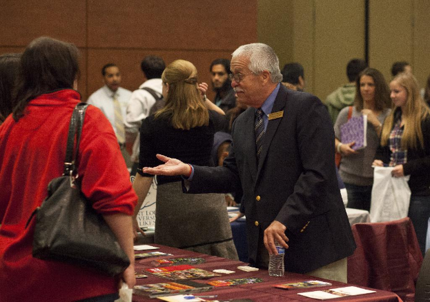 Ein voller Saal mit Menschen, Tischen mit Papieren und Zeitschriften und eine Wand im Hintergrund.