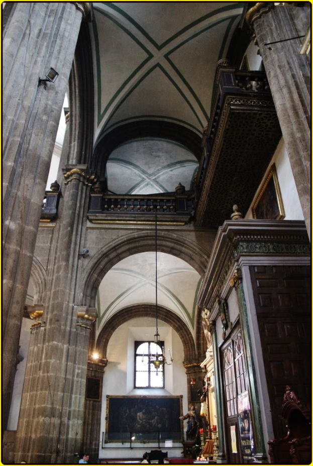 Ein prunkvoller Innenraum eines Palasts mit Schränken, beleuchteten Säulen, Wandskulpturen, einem großen Rahmenbild und einer von der Decke hängenden Lampe.