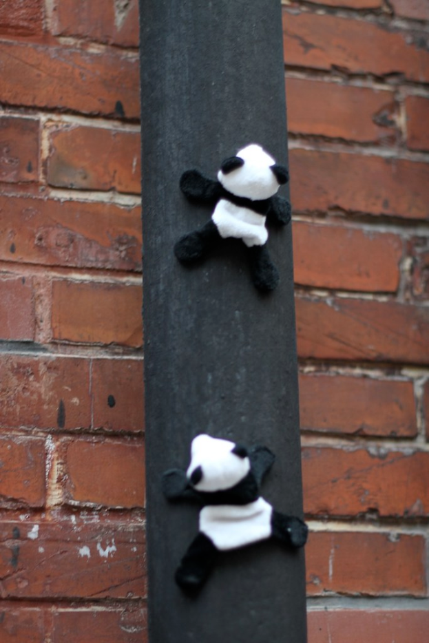Pandaspielfiguren an einem Holzpfahl vor einer Backsteinwand.