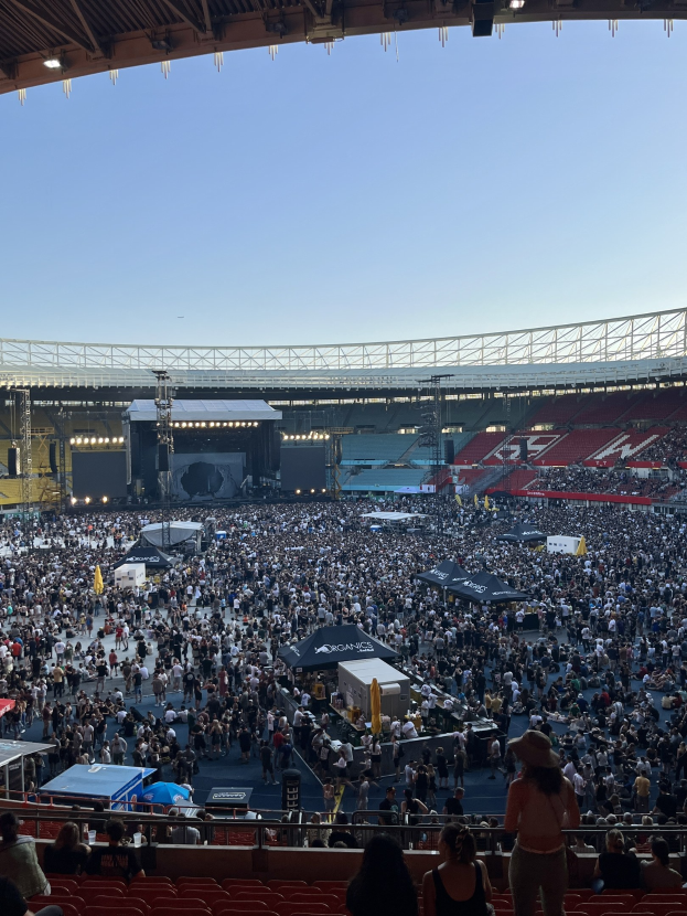 Große Menge sitzend und stehend in einer Halle mit Zelten, Geländern und Deckenbeleuchtung während eines Konzerts in der O2 Arena in London.