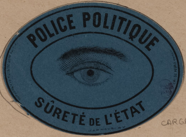 Brauner Karton mit blauem Aufkleber mit der Aufschrift "Polizei Politique Surete de L'Etat" und einem Auge-Symbol in der Mitte.