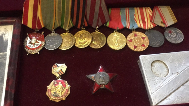 Eine hölzerne Box mit verschiedenen Medaillen, darunter ein roter Stern, ordentlich mit einem Objekt auf der rechten Seite angeordnet.