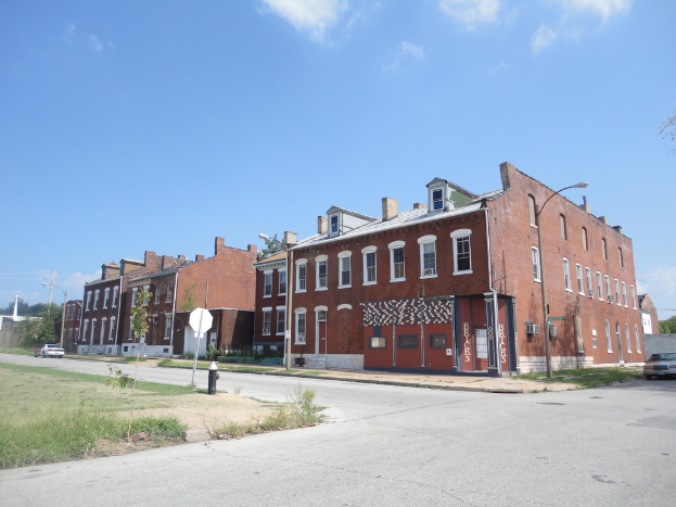 Ein Gebäude mit Masten und Straßenlampen, umgeben von Bäumen und Fahrzeugen auf beiden Seiten, mit einem Weg, Gras und einem Feuerlöscher unten und dem Himmel oben.